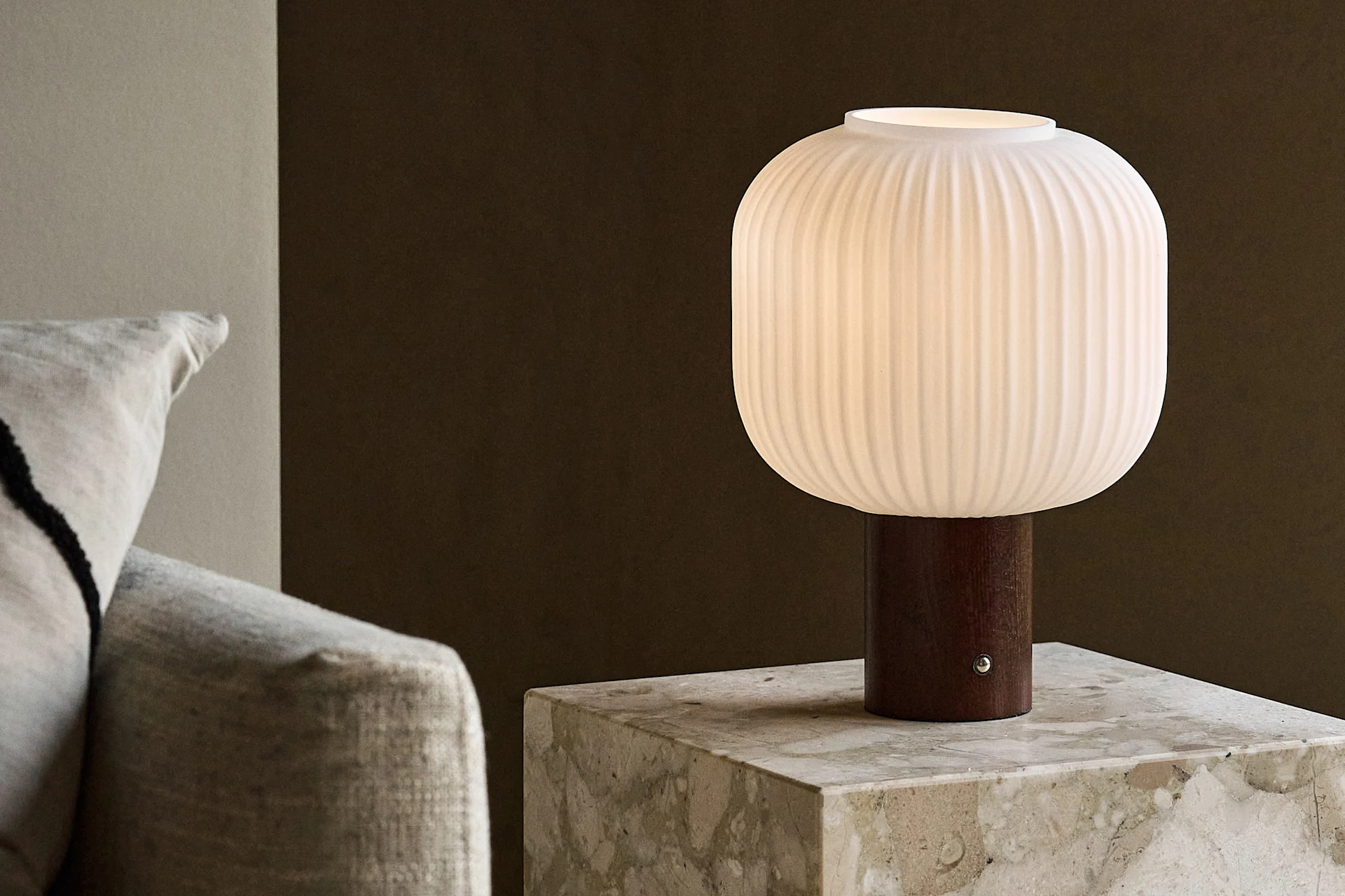 Biała prążkowana lampa stołowa z drewnianą podstawą na marmurowym stoliku bocznym obok sofy.